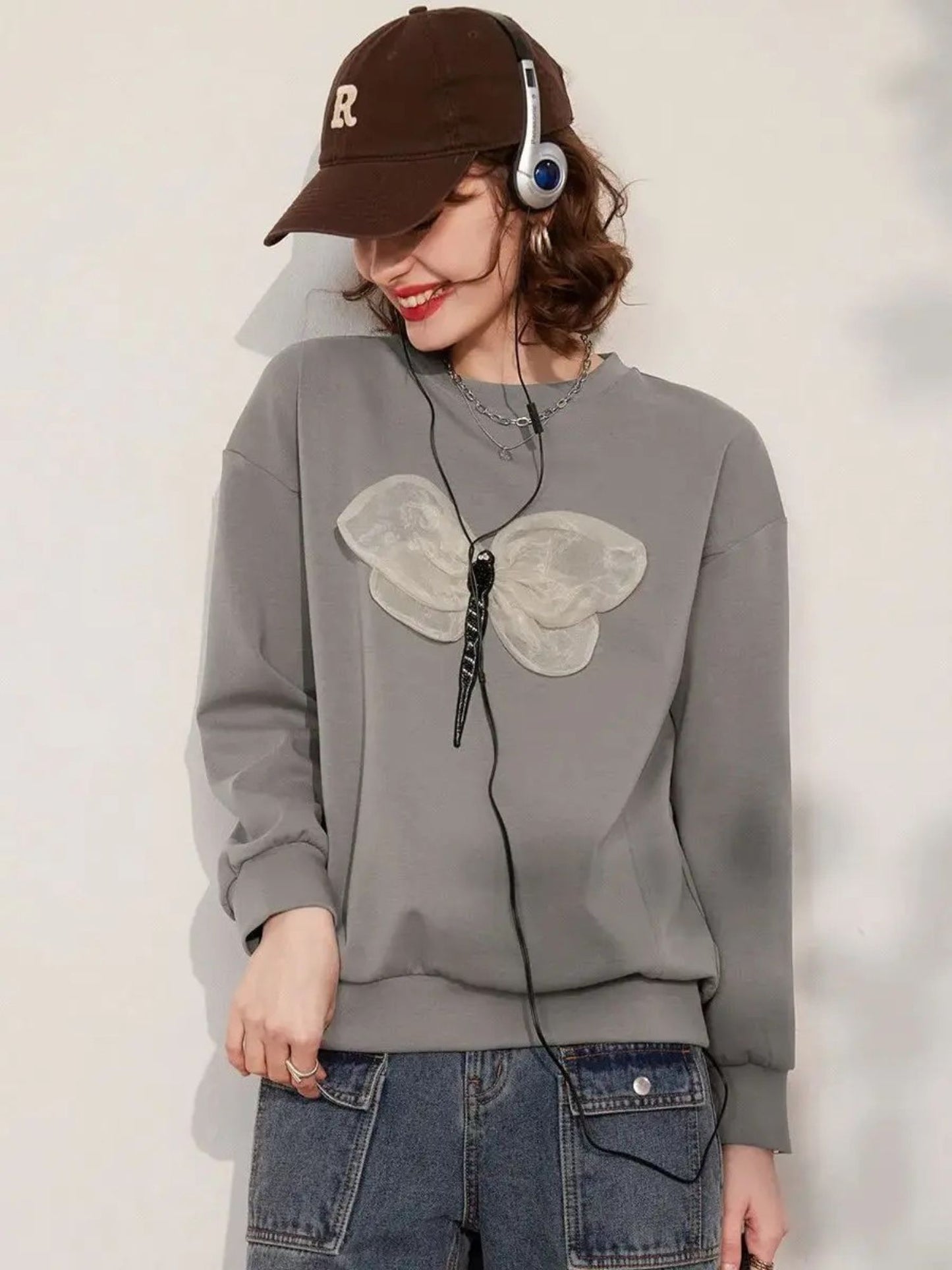 A woman wearing a grey jumper with a 3D dragonfly decoration on the front, paired with denim shorts