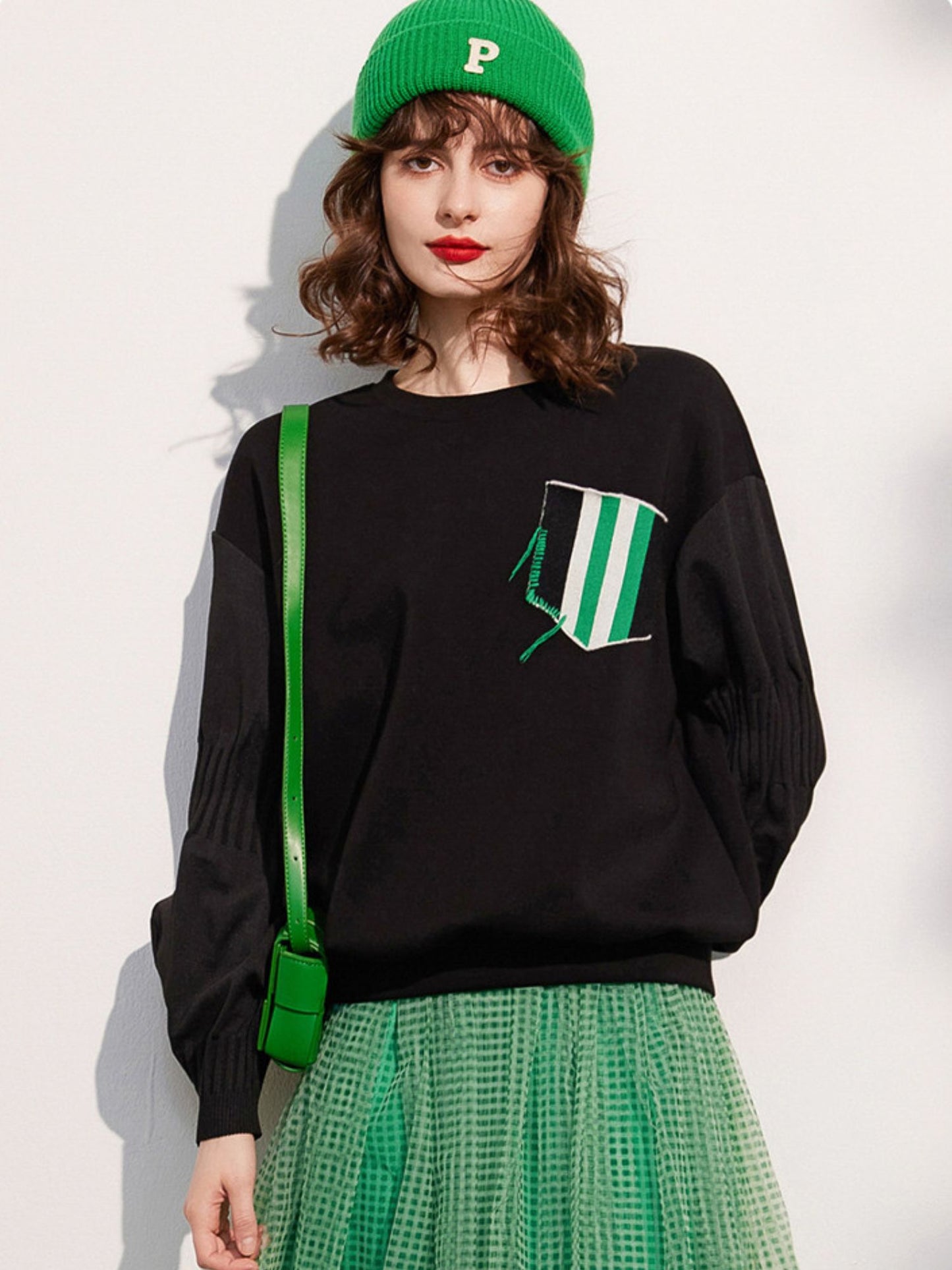 Full view of the woman in a green beanie, black sweatshirt, and green skirt, standing and facing forward
