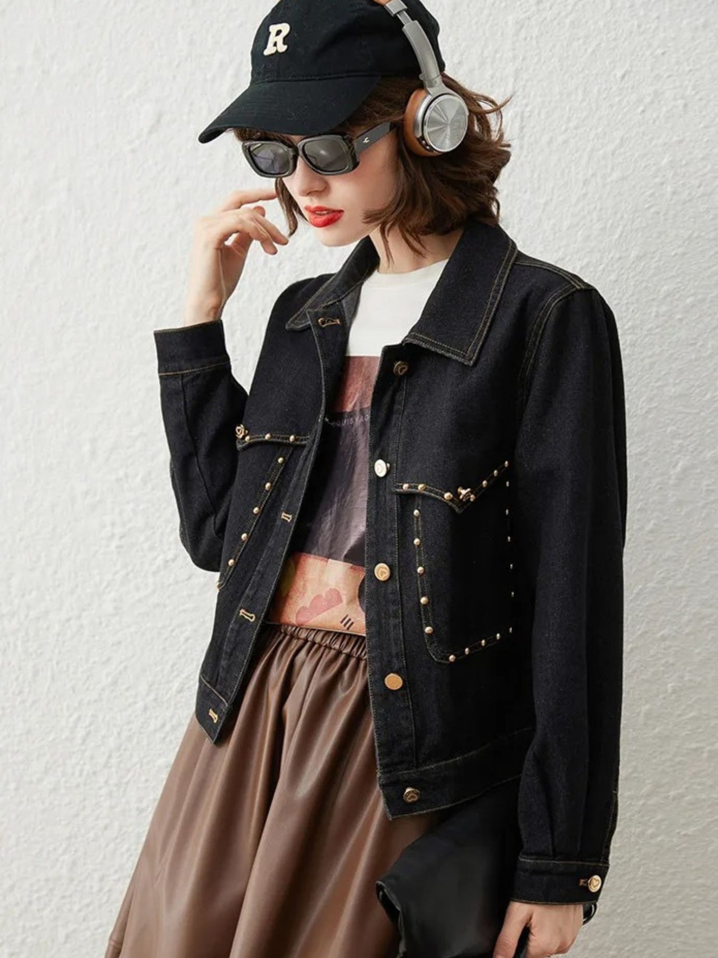 Woman in black denim jacket, sunglasses, and headphones, smiling with relaxed pose