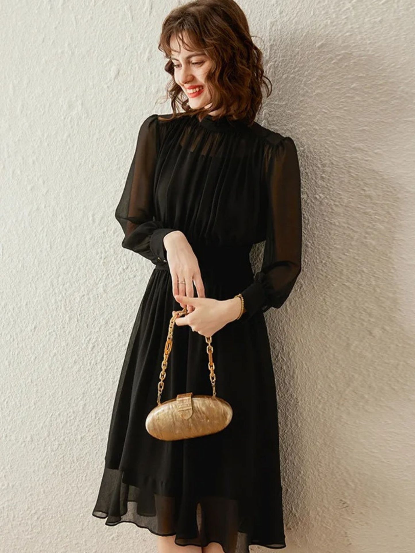 Woman holding gold handbag while wearing black pleated midi dress
