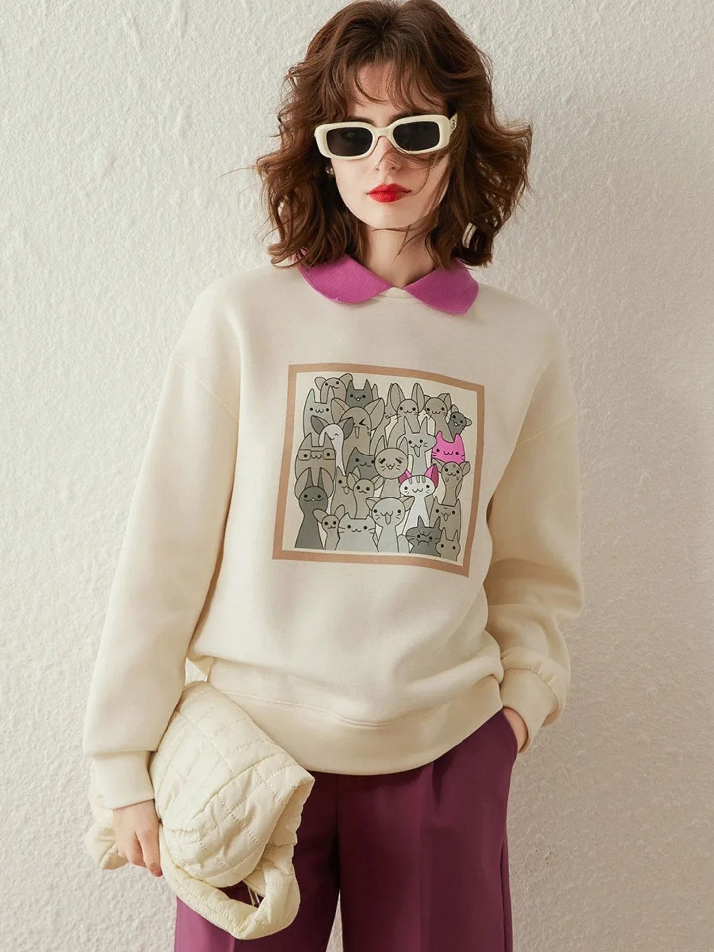 Woman wearing an ivory sweatshirt with graphic print, styled with pink collared shirt and skirt, holding a clutch