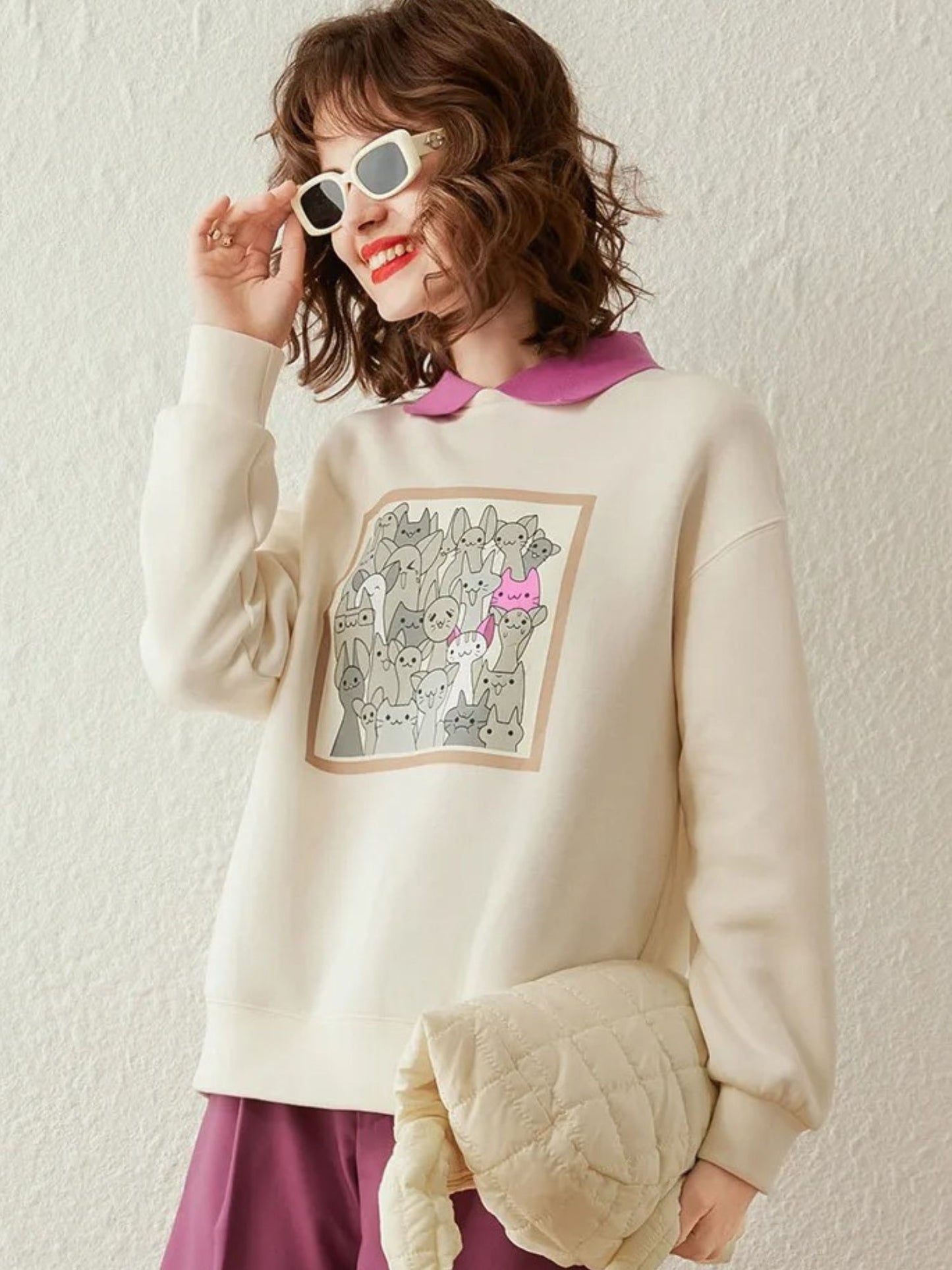 Woman in ivory sweatshirt with front design, smiling with sunglasses