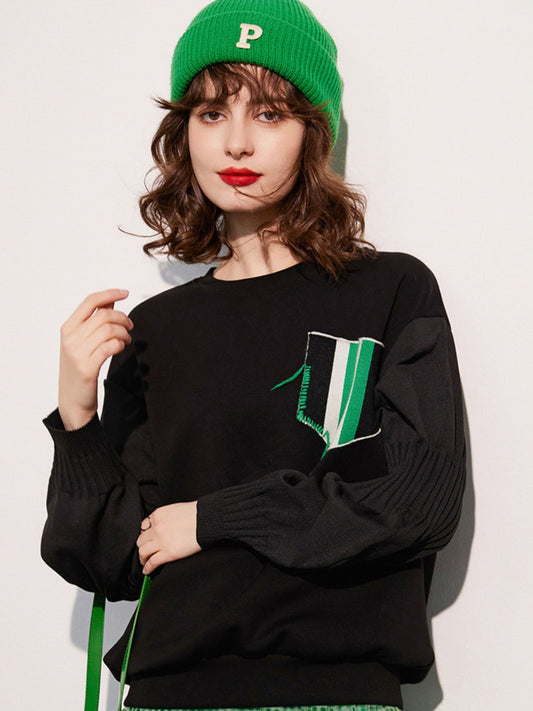 Woman wearing a green beanie and a black sweatshirt with a green-and-white design on the chest, posing against a white background